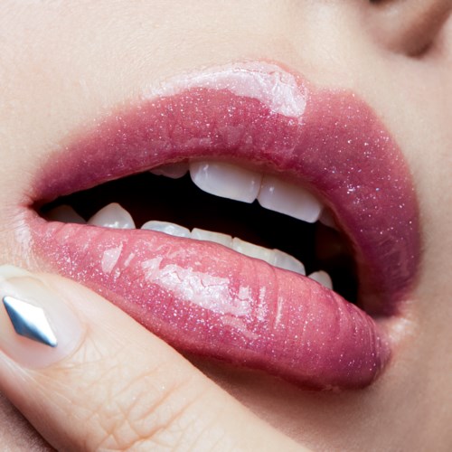 Nærbilde av lepper med rosa gloss og noe hvitt, finger som berører leppene.