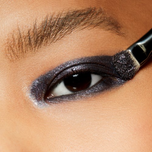 En person använder en borste för att applicera svart ögonskugga på ögonlocket och skapar en smoky eye look.