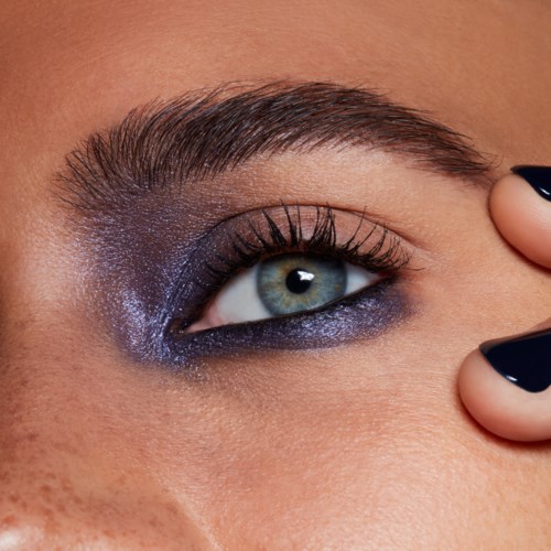 Nahaufnahme eines Frauenauges mit kräftigem lila Lidschatten, langen Wimpern und gepflegtem Augenbrauen.