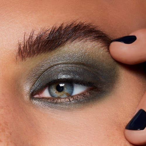 Nahaufnahme eines Auges mit dunklem Make-up, einschließlich Lidschatten und Eyeliner, sowie gepflegte Augenbrauen.