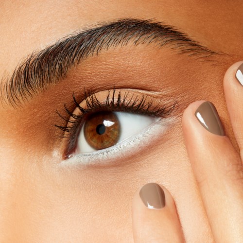 Close-up van een persoon haar oog met goed verzorgde wenkbrauwen en netjes geverfde nagels. De persoon raakt het ooglid aan.