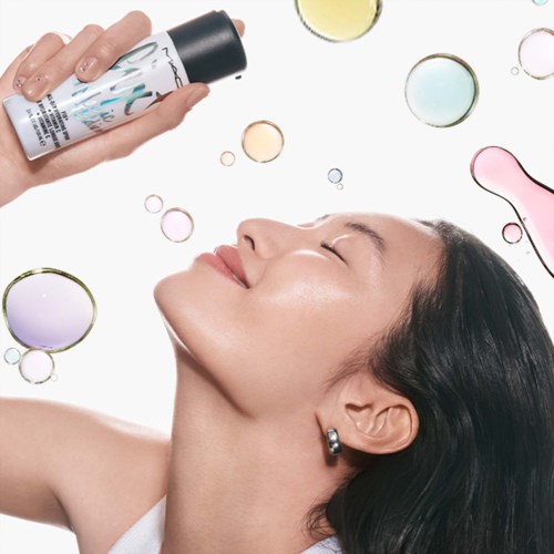 En kvinna njuter av en hudvårdspray bland färgglada bubblor, med ett glatt, avkopplat ansikte och stängda ögon.