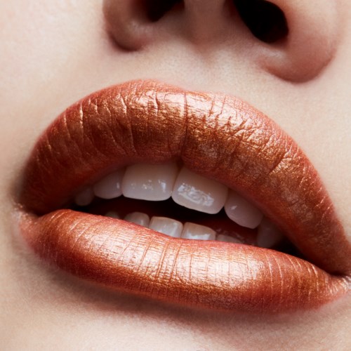 Close-up van lippen met glanzende, metallic koperkleurige lipstick en zichtbare tanden.
