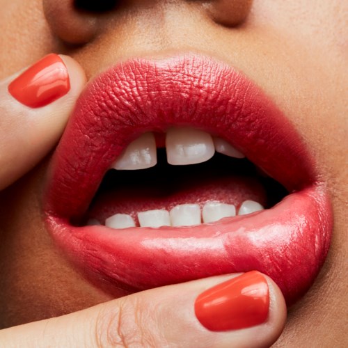 Close-up van lippen, licht geopend, toont tanden en rode nagellak. De lippen zijn glad en roze.