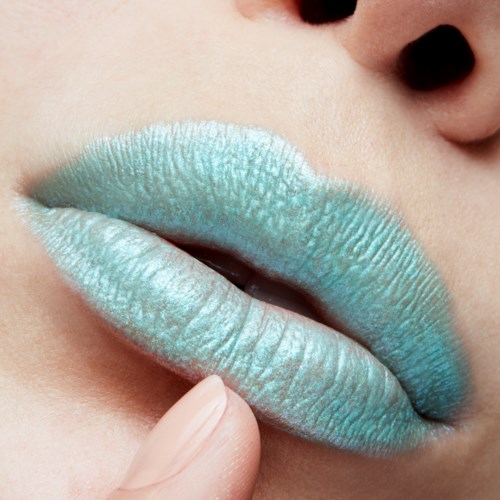 Close-up van lippen met groenblauwe lippenstift, die de onderlip voorzichtig aanraakt.