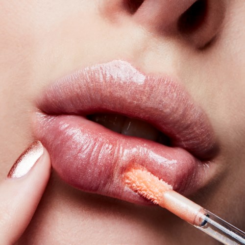 En person påfører leppestift eller lip gloss med en liten børste. Nærbilde, fokus på lepper og hånd.