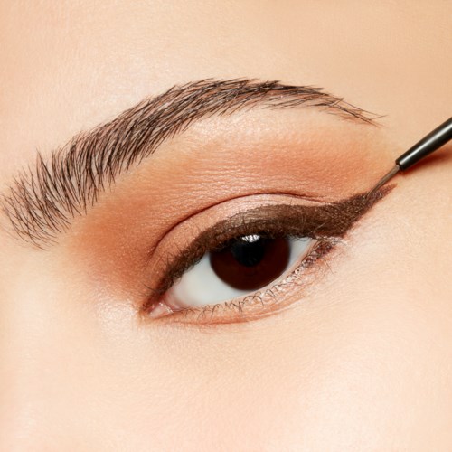 En person använder en tunn pensel för att måla eyeliner på ögonlocket, fokuserar på ögonmakeup.
