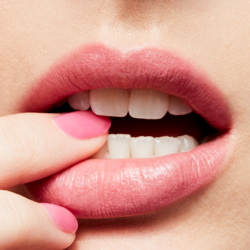 Nahaufnahme von Lippen, mit Finger berührt Unterlippe, zeigt weiße Zähne und rosa Lippenstift.