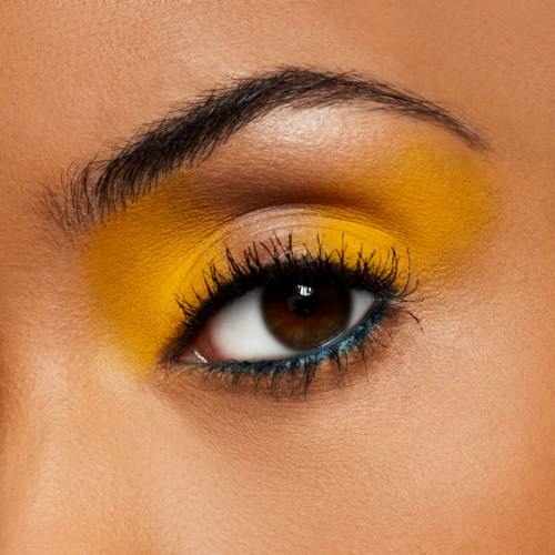 Närbild av ett öga med gul ögonskugga, svart eyeliner och långa ögonfransar.