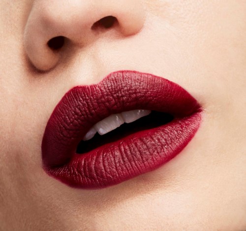 Nahaufnahme von den Lippen einer Person mit dunkelrotem Lippenstift, zeigt leicht gespaltene Lippen und teilweise Zähne.