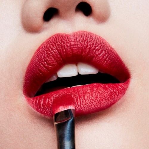 Eine Person trägt leuchtend roten Lippenstift auf, die Lippen sind leicht geöffnet und zeigen weiße Zähne.