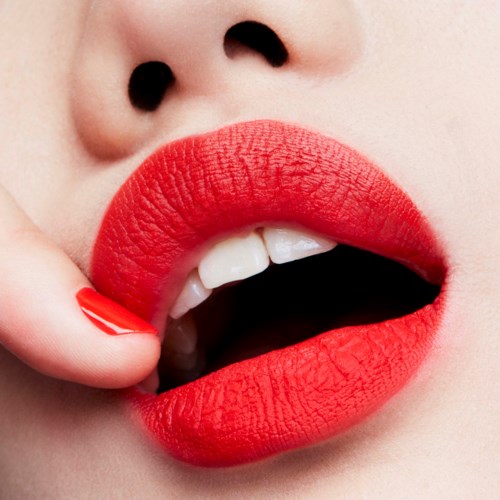 Nahaufnahme von Lippen mit rotem Lippenstift, leicht geöffnet, zeigt Zähne, glatte helle Haut.