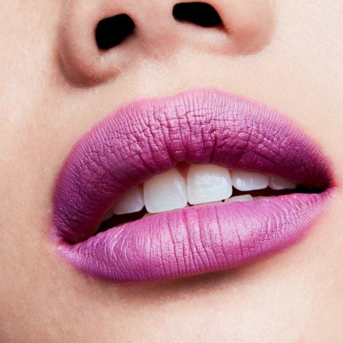 Nahaufnahme von Lippen mit lila und pinkem Lippenstift, leicht geöffnet, zeigt Zähne.