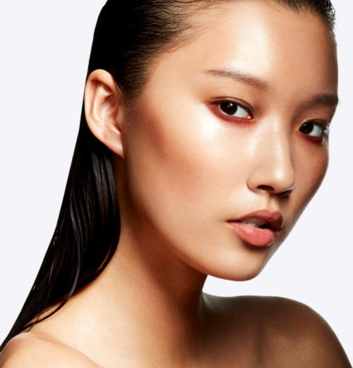 A close-up of a woman with smooth skin and long, dark hair, looking confidently at the camera.