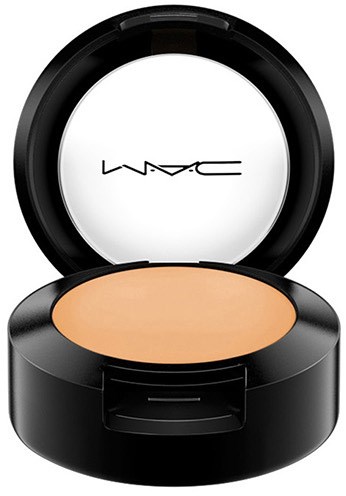 En MAC-sminkkompakt med beige puder och lock öppet som visar MAC-loggan på spegeln.