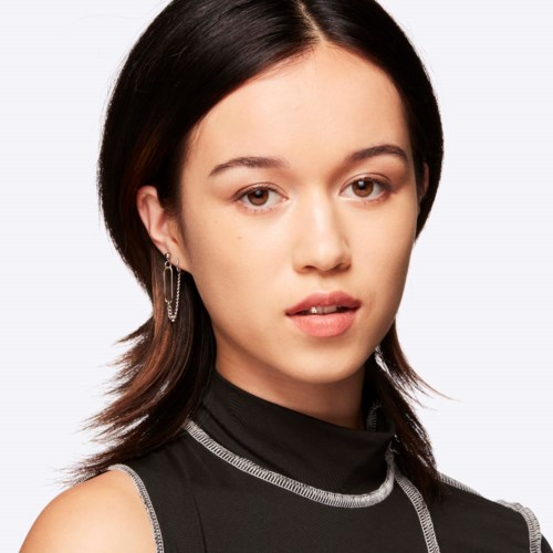 En kvinde med sort hår og øreringe har på sig en sort turtle-necks bluse med sølvdetaljer.
