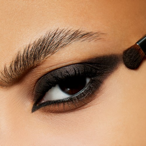 Nahaufnahme eines Auges mit dunklem Lidschatten und einem Make-up-Pinsel, der schwarzen Lidschatten aufträgt.