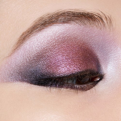 Close-up van een oog met roze, paarse en zwarte oogschaduw en goed verzorgde wenkbrauw.