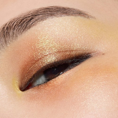 Close-up van een oog met glanzende gouden oogschaduw en winged eyeliner. Wenkbrauw is mooi gevormd.