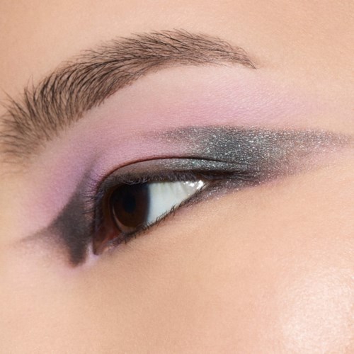 Close-up van een oog met pastelroze en glinsterende blauwe oogschaduw en verzorgd wenkbrauw.