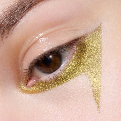 Nærbilde av et øye med gullglitter øyemakeup og et gull lynmønster under øyet.