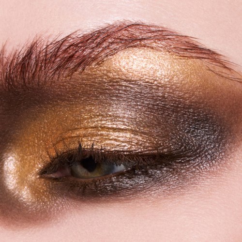 Nærbilde av et øye med gull-, svart og glitrende makeup, og synlige øyenbrynshår.