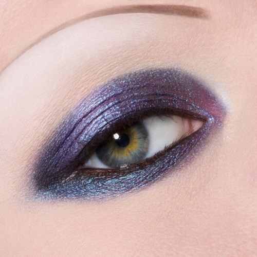 Close-up van een menselijk oog met levendige paarse en blauwe oogschaduw en zwarte eyeliner.