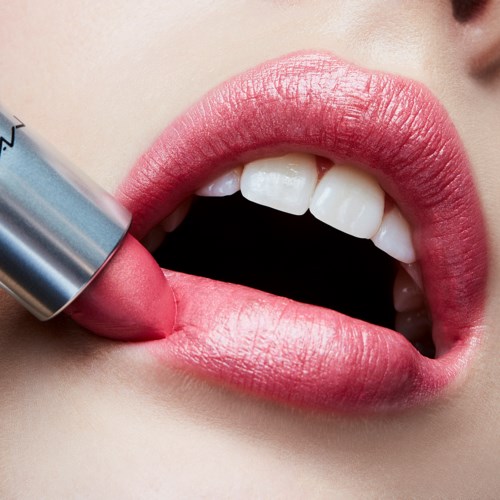 Een persoon brengt roze lippenbalsem aan op de lippen, dicht bij gezicht en tanden. De lippen zien er glad en glanzend uit.