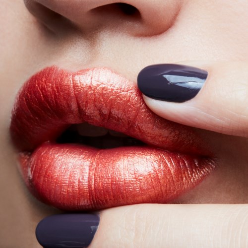 Close-up van lippen met rode, glanzende lippenstift en een vinger met donkere nagellak die de lippen aanraakt.