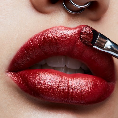 Close-up van lippen die rood lippenstift krijgen met een kleine kwast, boven de lippen zie je een piercing.