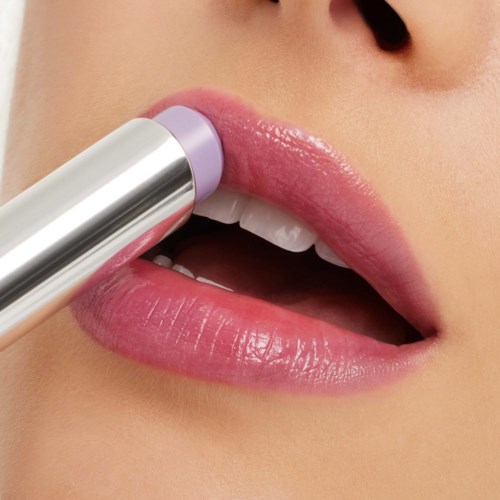 Iemand brengt lichtpaarse lippenstift aan op de lippen, die licht geopend zijn en witte tanden tonen.