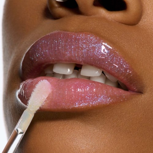Close-up van lippen met glanzende roze gloss, een lipbrush brengt gloss aan, laat tanden en een egale huid zien.