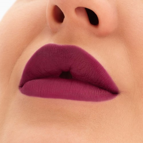 Close-up van lippen met donkerpaarse lipstick en kleine opening tussen lippen. Huid eromheen is licht.