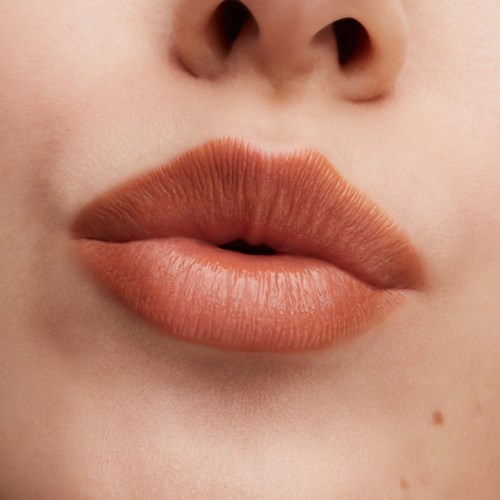Close-up of lips with soft peach lipstick, slightly parted, showing smooth skin around.