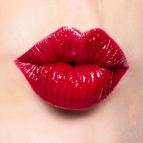 Close-up of lips with shiny, bright red lipstick, slightly parted. Smooth skin surrounds the lips.