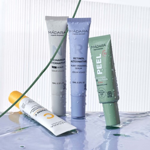 Four skincare tubes stand upright on a reflective surface, with a green leaf and a yellow ball nearby.