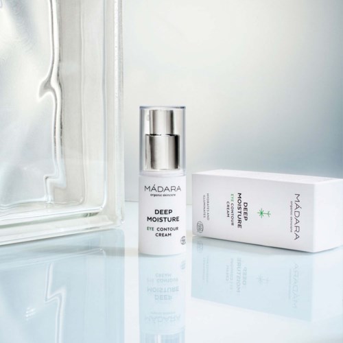 Ein Hautpflegeprodukt namens Madara Deep Moisture Eye Contour Cream mit seiner Verpackung, auf einer hellen Oberfläche.