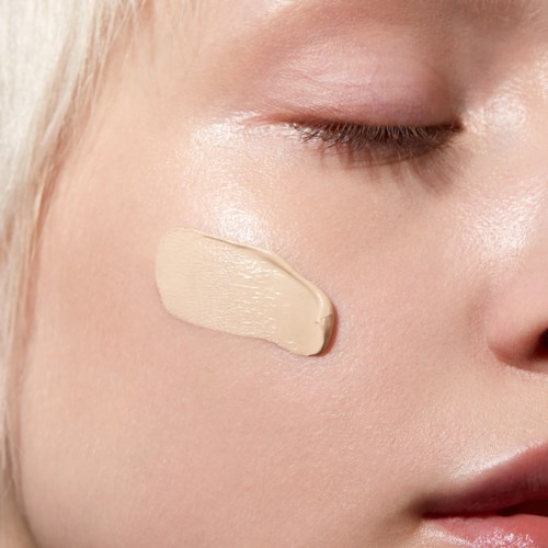 Närbild av en persons ansikte med ett stryk av beige foundation eller concealer på kinden.