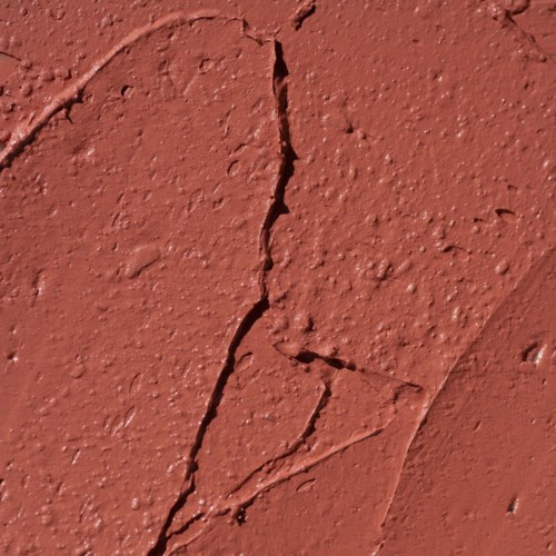 Gekerfde roodbruine muur met kleine bobbels en ruwe textuur.
