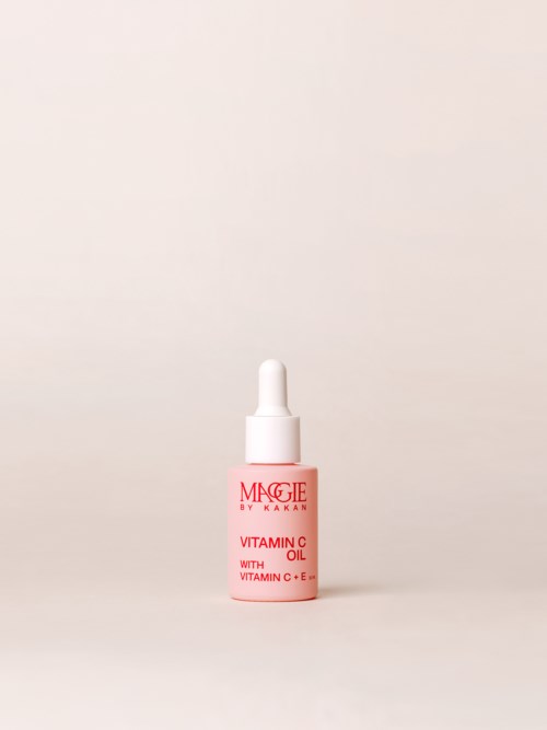 En liten rosa flaska märkt 'MAGIE by KAKAO' innehåller vitamin C-olja, med en pipettlock, på en enkel bakgrund.