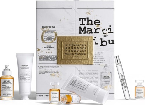 A collection of Maison Margiela Replica perfume bottles and skincare products with a white branded box behind them.