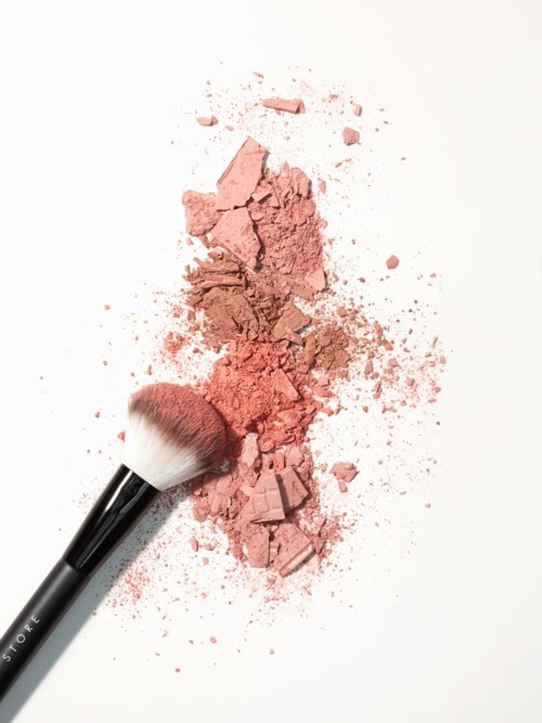 En makeupborste med rosa pulver spritt på en vit yta.