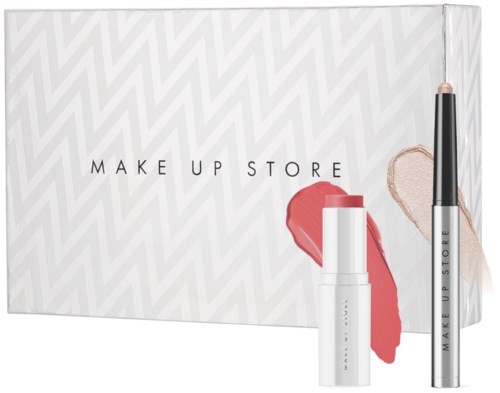 Pudełko z produktami do makijażu, w tym szminką i korektorem, na wzorzystym tle. Pudełko ma tekst "MAKE UP STORE."