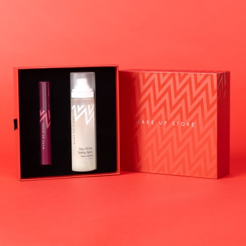 Et makeup-set i en rosa eske inkluderer en leppestift og en setting spray.