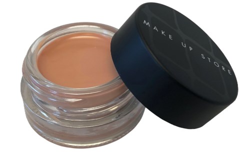 En lille glas med beige makeup-kræmmer med sort låg mærket "MAKE UP STORE."