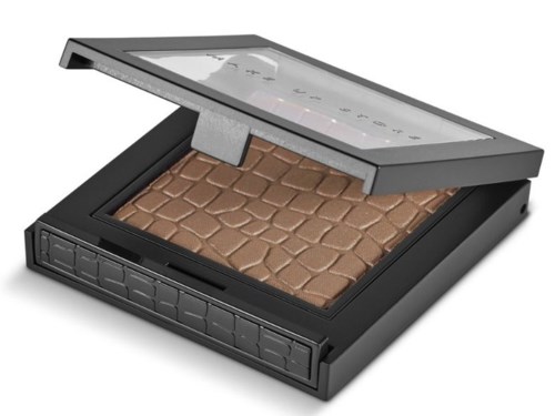 A makeup compact with brown pressed powder inside, and a clear lid showing some text and graphics.