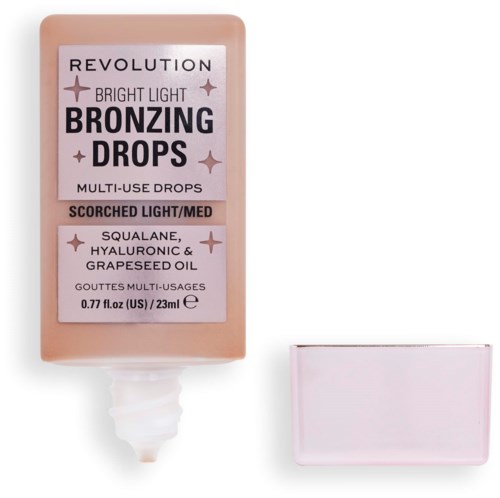 En flaska Revolution Bright Light Bronzing Drops med en liten spegel bredvid.