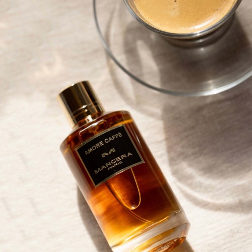 En flaske Amore Caffé Mangera Paris parfum ligger på en overflade, med et glas i nærheden.