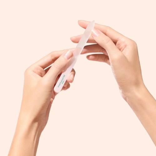 Händer som håller en vit tub, troligen en hudvårds- eller kosmetikprodukt, med en mjuk beige bakgrund.