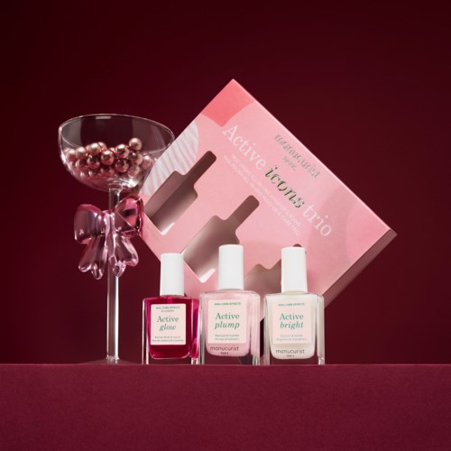A set of three skincare bottles with a decorative pink bow, a pink box, and a glass containing pink beads.